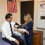 Man in white shirt gets blood pressure check from student in blue scrubs